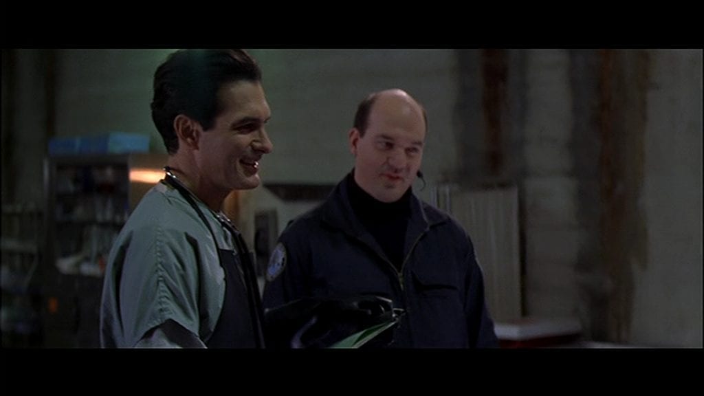 Joe Bob Briggs in the film Face-Off, playing a coroner standing next to cop. 