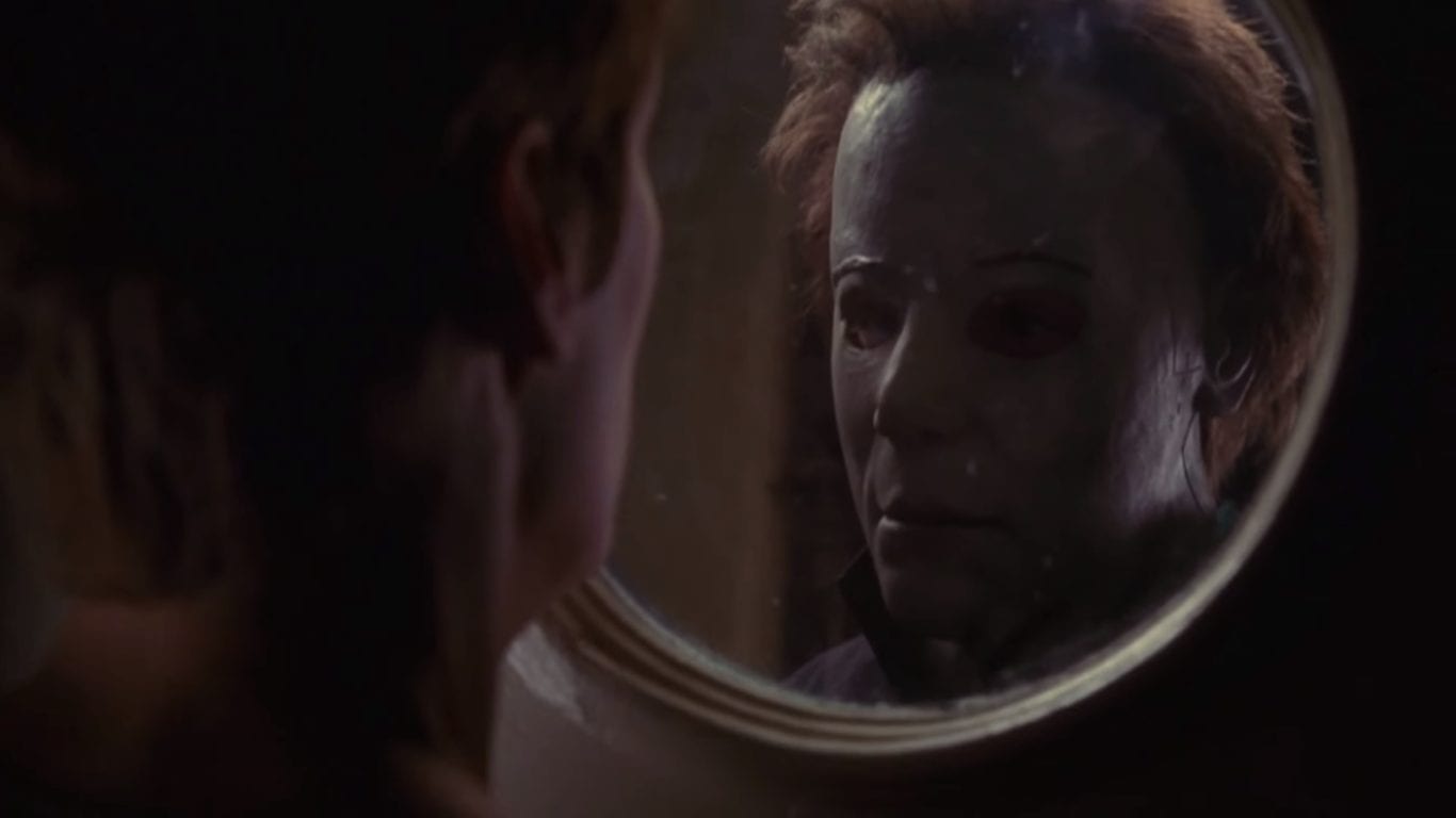 Michael Myers looks at his masked face in a mirror