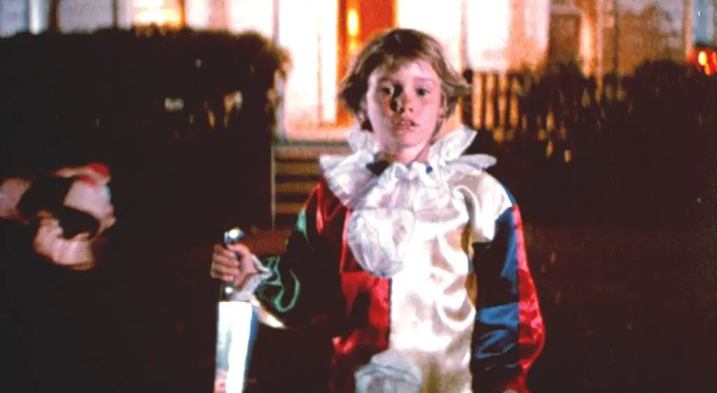 a boy dressed as a clown brandishes a large knife