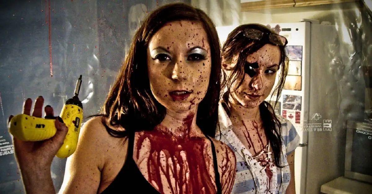 Two women splattered in blood, one holds a power tool.