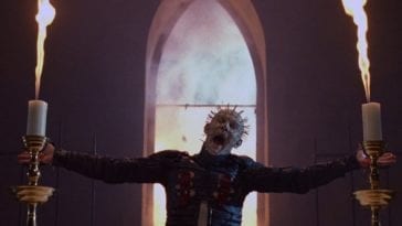 Pinhead stands in front of a church window.