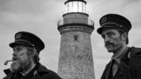two men stare out into the sea with a lighthouse in the background