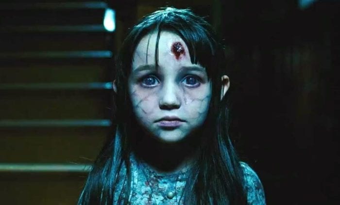 The ghost of a dead girl named Jodie with a bullethole in her forehead stands in the front hallway of a haunted house in The Amityville Horror (2005).