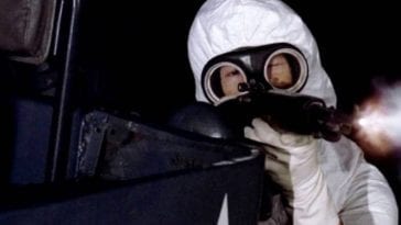 An army man wearing a white suit and gas mask points a gun at people