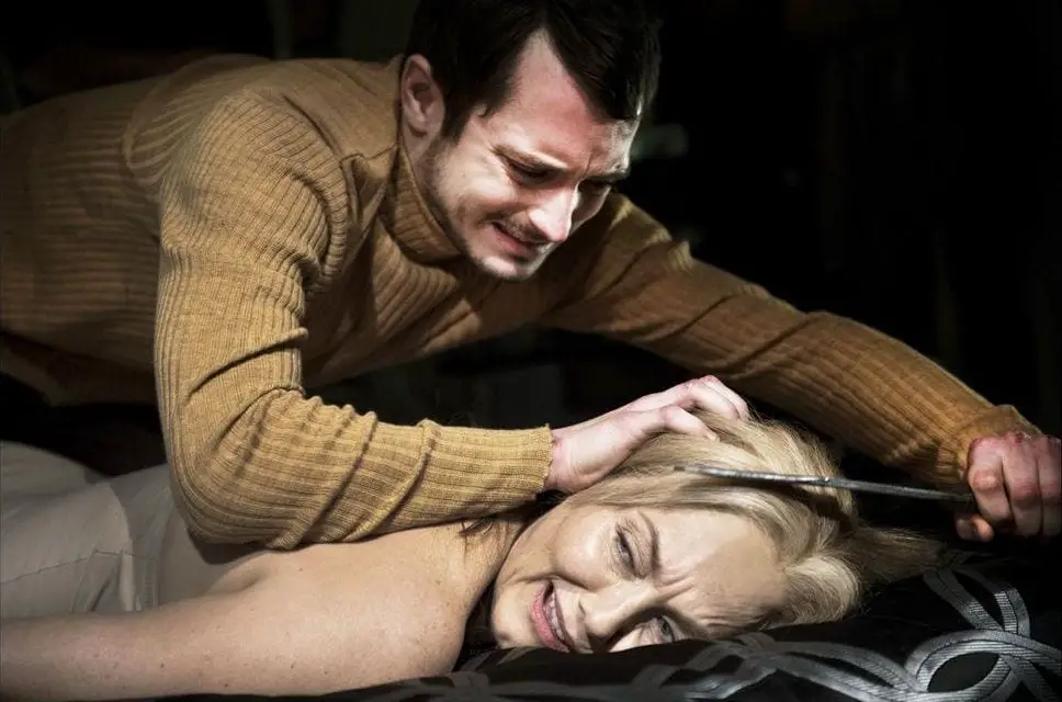Frank (Elijah Wood) sits on a naked victims back as he cuts her hairline with his knife.