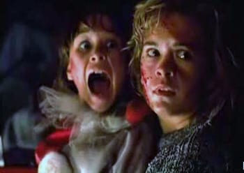 A young girl in a clown costume and teenage girl, both bloody, scream in horror while sitting in a truck.