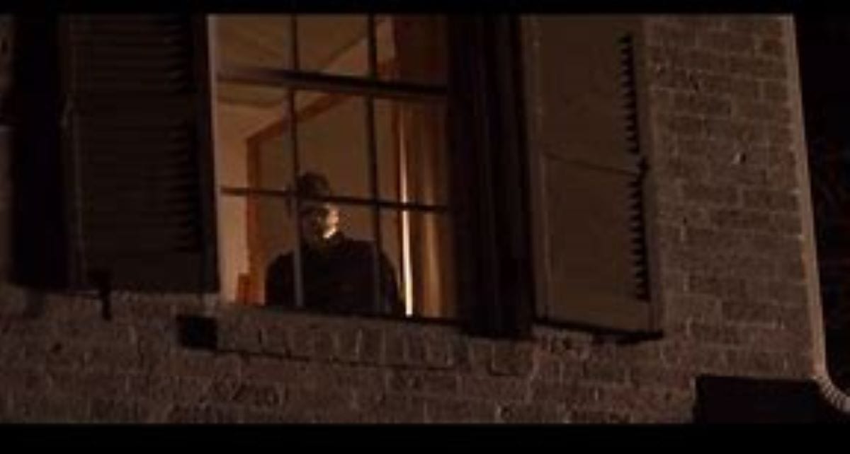 The killer Michael Myers stands in a bedroom window in Halloween