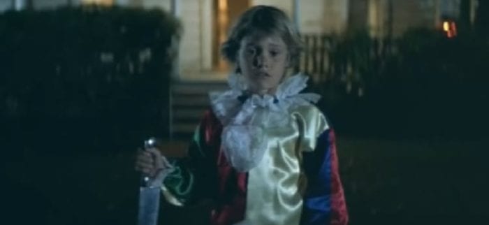A young boy, Micheal Myers stands catatonic holding a kitchen knife in a clown suit