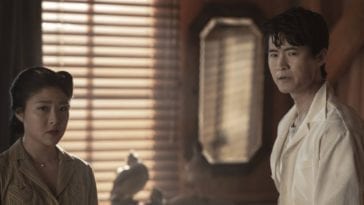 Amy and Ken stand in the barracks looking at someone off-screen with trepidation