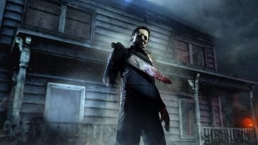 Michael Myers stands outside a dark house holding his bloody knife in front of him as a pumpkin shines in the background