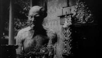 A horned demon in black and white sticks his tongue out while looking into the camera in Haxan