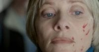 Barbara Crampton has blood on her face and stares off in the distance in We Are Still Here