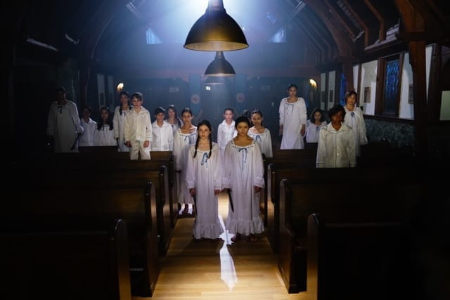 A bunch of possessed kids in white pajamas stand in a chapel.