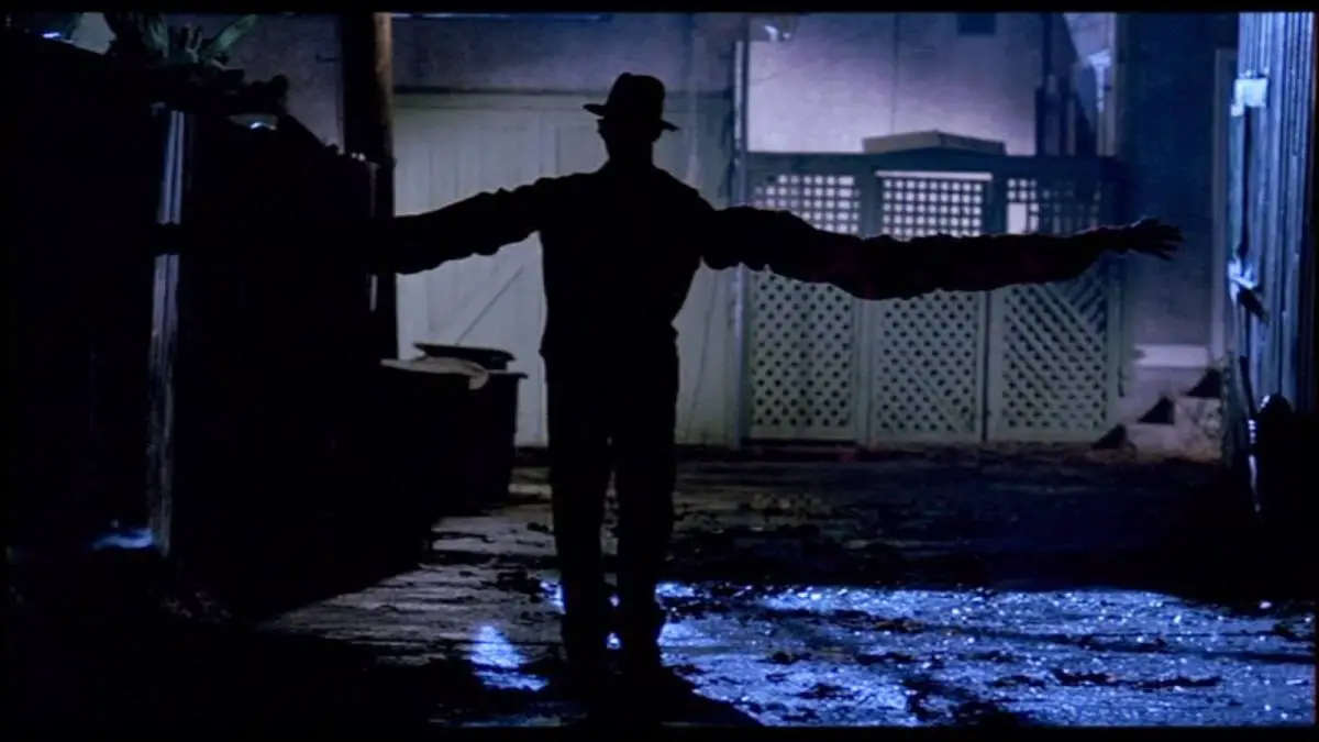 Freddy Krueger with extended arms walking down an alleyway at night