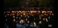 The Japanese citizens watch from the riverbank as lanterns float across the water