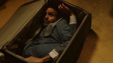 A man is contorted inside a suitcase, looking up frightened.