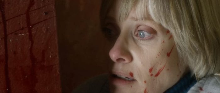Barbara Crampton has blood on her face as she stares out of a window in We Are Still Here