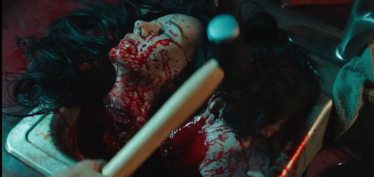 A hammer is held above two bloody severed heads.