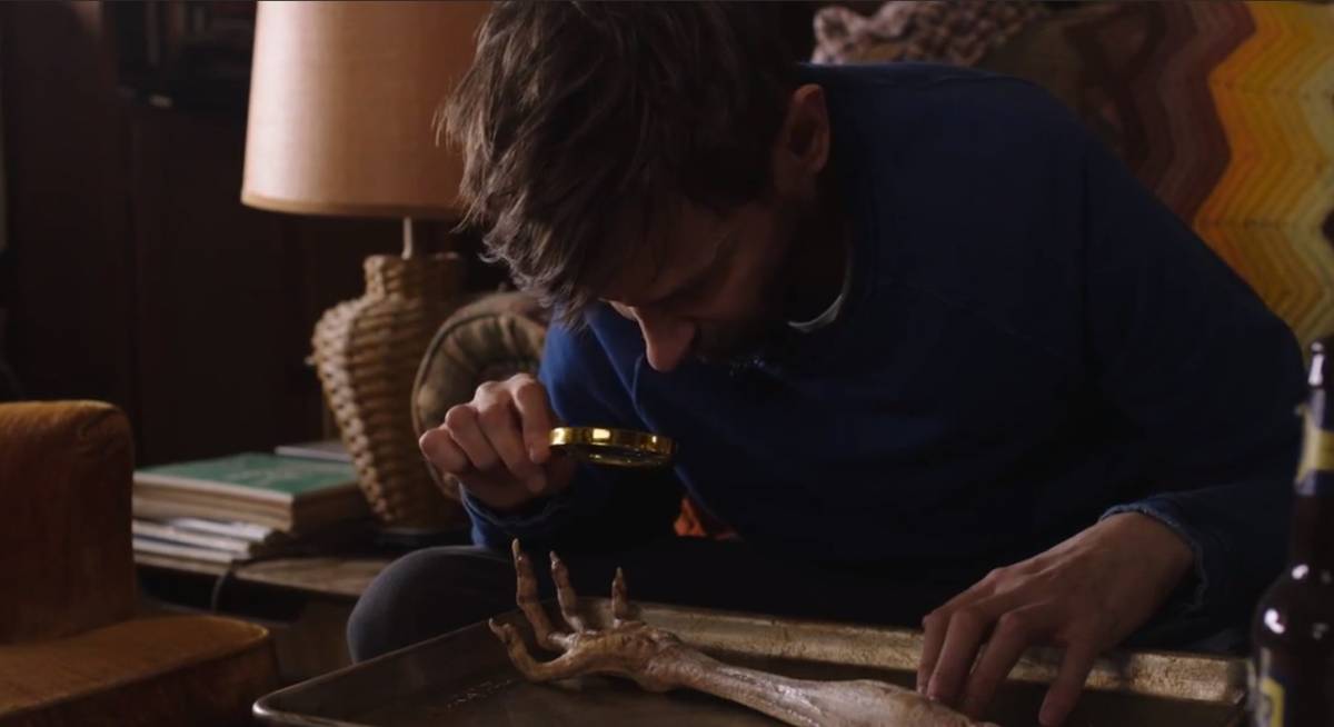 Clark examines the a mysterious four-fingered hand with claws on his coffee table using a magnifying glass.