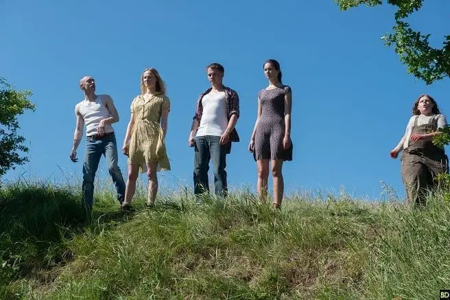 The five main characters, two women and three men, stand on a grassy hill.