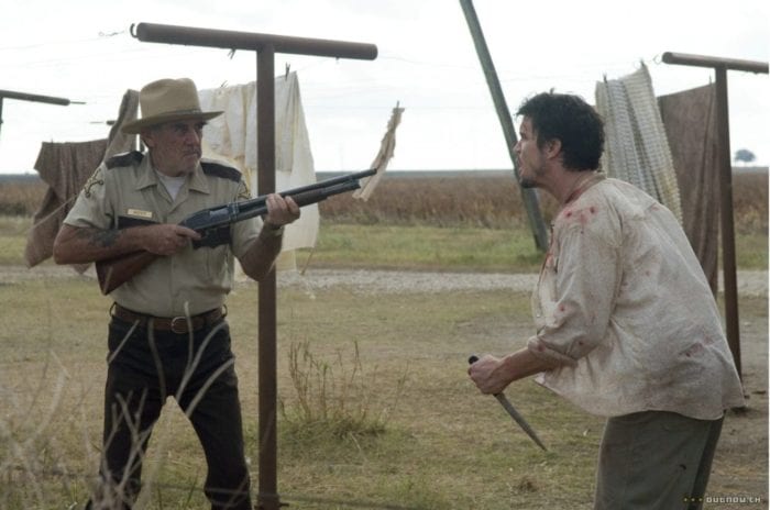 R. Lee Emery's character points a shotgun at one of the other characters, who is yelling and wielding a knife