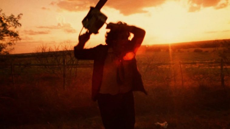 Leatherface sings his chainsaw in frustration on a road while the sun sets