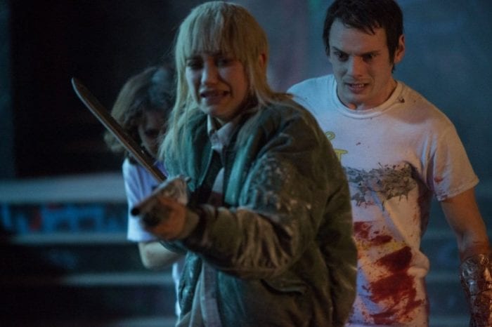 Amber brandishes a shotgun with a distressed look on her face while Pat and Sam hide behind her.
