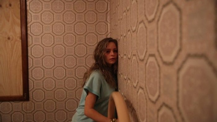 Vicki leans against a wall trying to listen to what is being said on the other side.