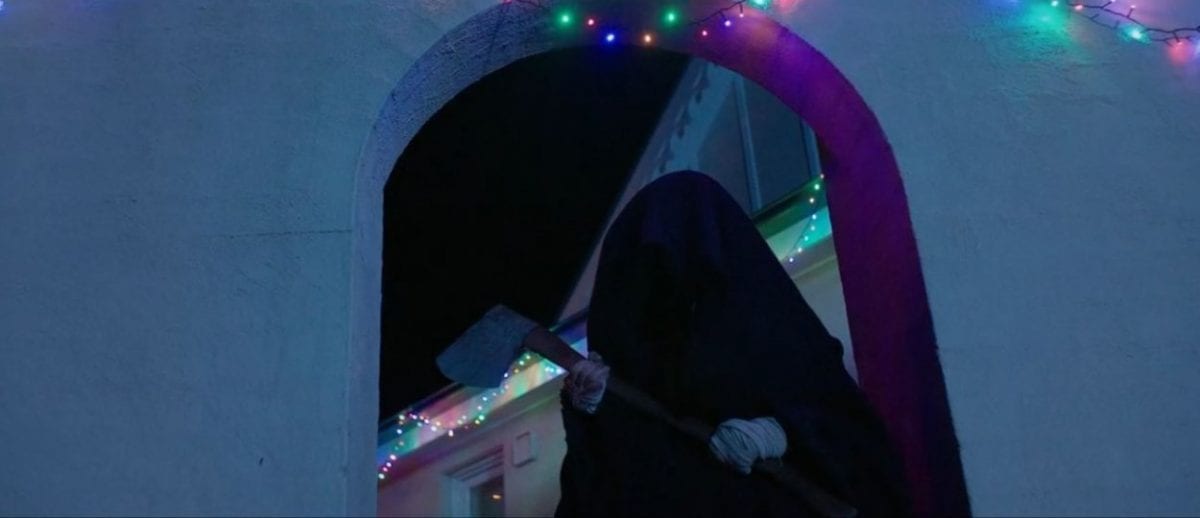 Cletus stands in a black cloak and holds an ax outside of the house in Red Christmas