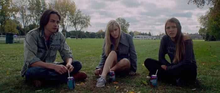 Maika Monroe's Jay, Lili Sepe's Kelly, and Daniel Zovatto's Greg sit in a semi circle watching someone off screen explain the mystery of the Follower