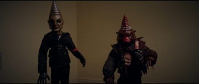 Two evil dolls with cone heads stare at the camera. 