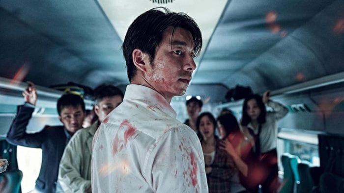 main character seok-woo looking behind him, covered in blood. passengers of the train stare in the same direction behind him.