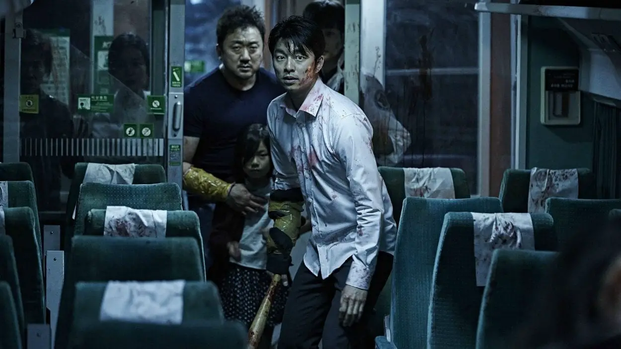 main characters seok-woo, su-an, and sang-hwa carefully walking through a train car, with sang-hwa carrying a bat