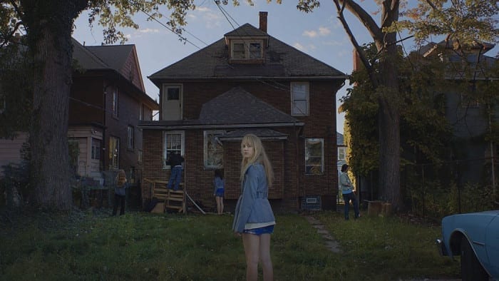 Jay stands at the back of a run down home as her friend investigate the property.