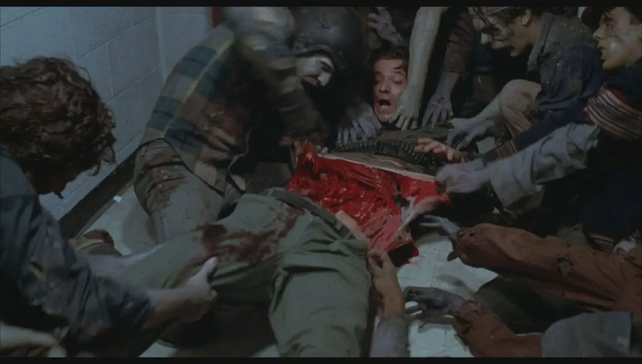 A man lies on the ground surrounded by zombies who are tearing into his flesh, ripping his torso apart