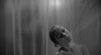 Marion Crane showering in the foreground, while behind the shower curtain, a figure approaches in the background.