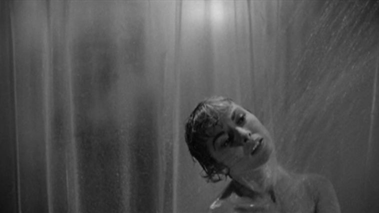 Marion Crane showering in the foreground, while behind the shower curtain, a figure approaches in the background.