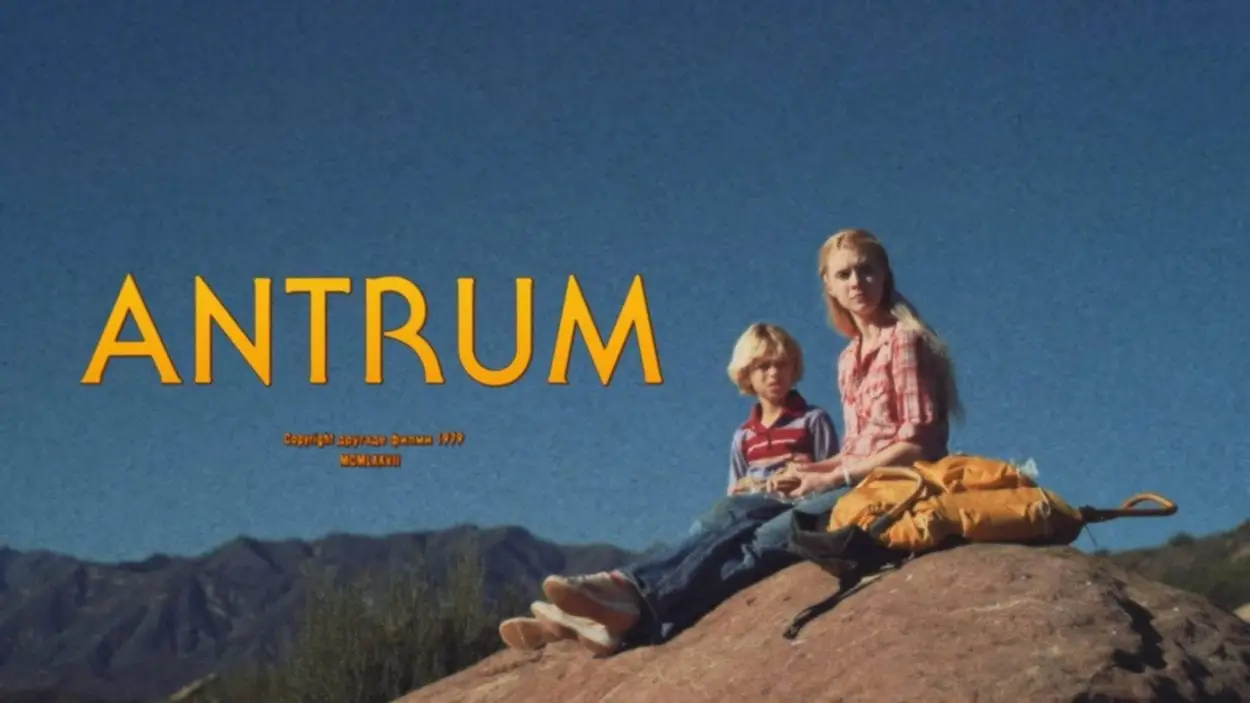 Screenshot showing The title Antrum and a young boy and his older sister sitting on top of a rock ledge with mountains visible in the background