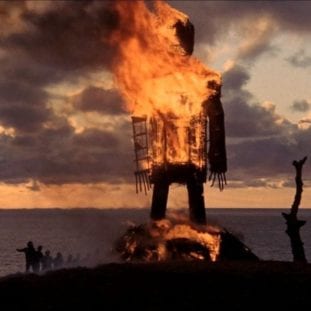a large wicker man burns on the top of a hill