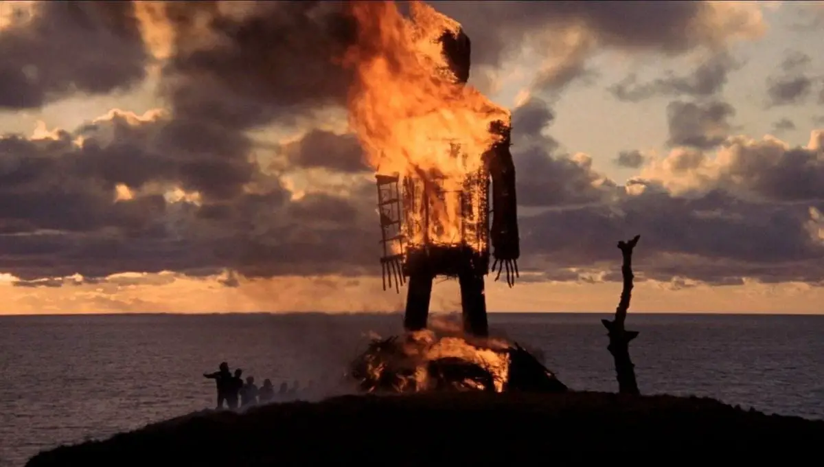 a large wicker man burns on the top of a hill