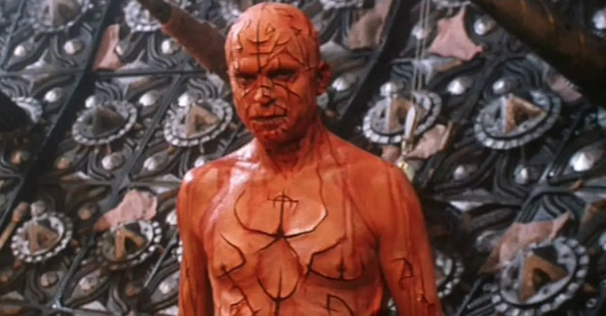 A shirtless man with symbols carved into his face and body.