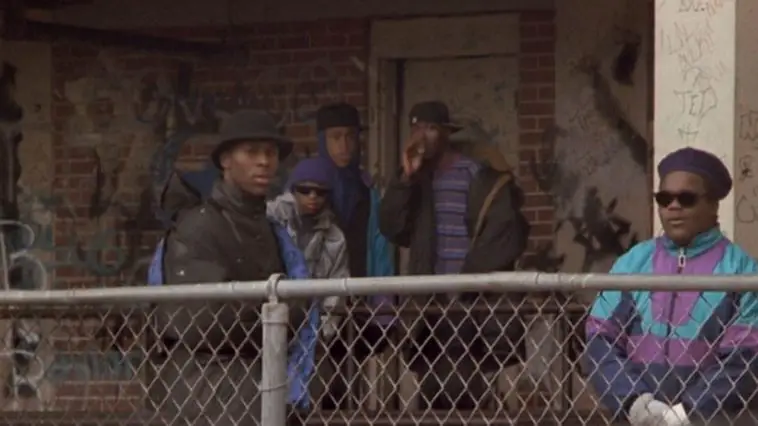 Five young black males stand behind a chain-link fence near a housing complex