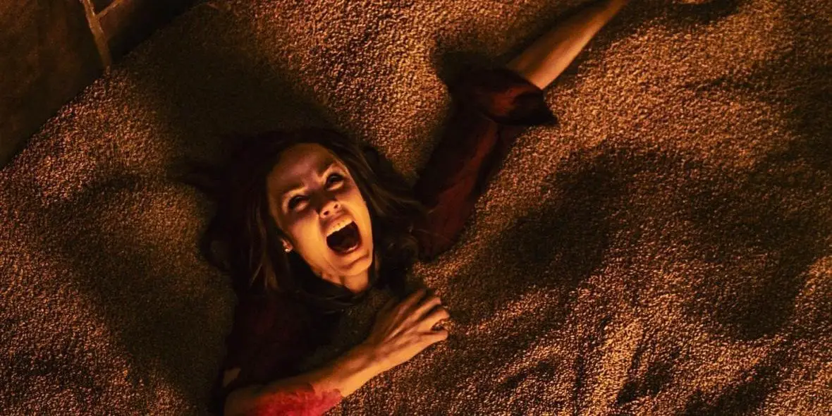 Bloody woman screams as she sinks into a sand pit.