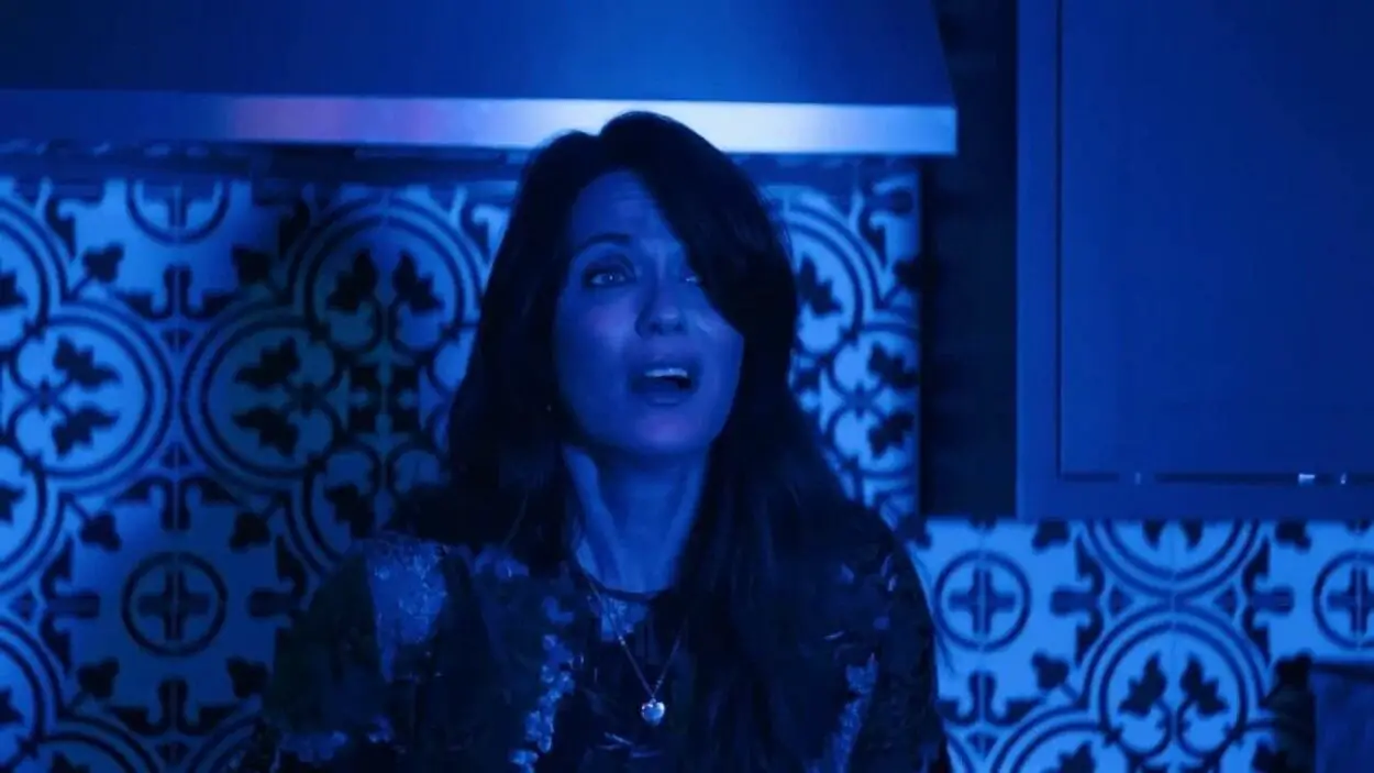 long haired woman facing the camera looking off in the space in front of her bathed in a blue light