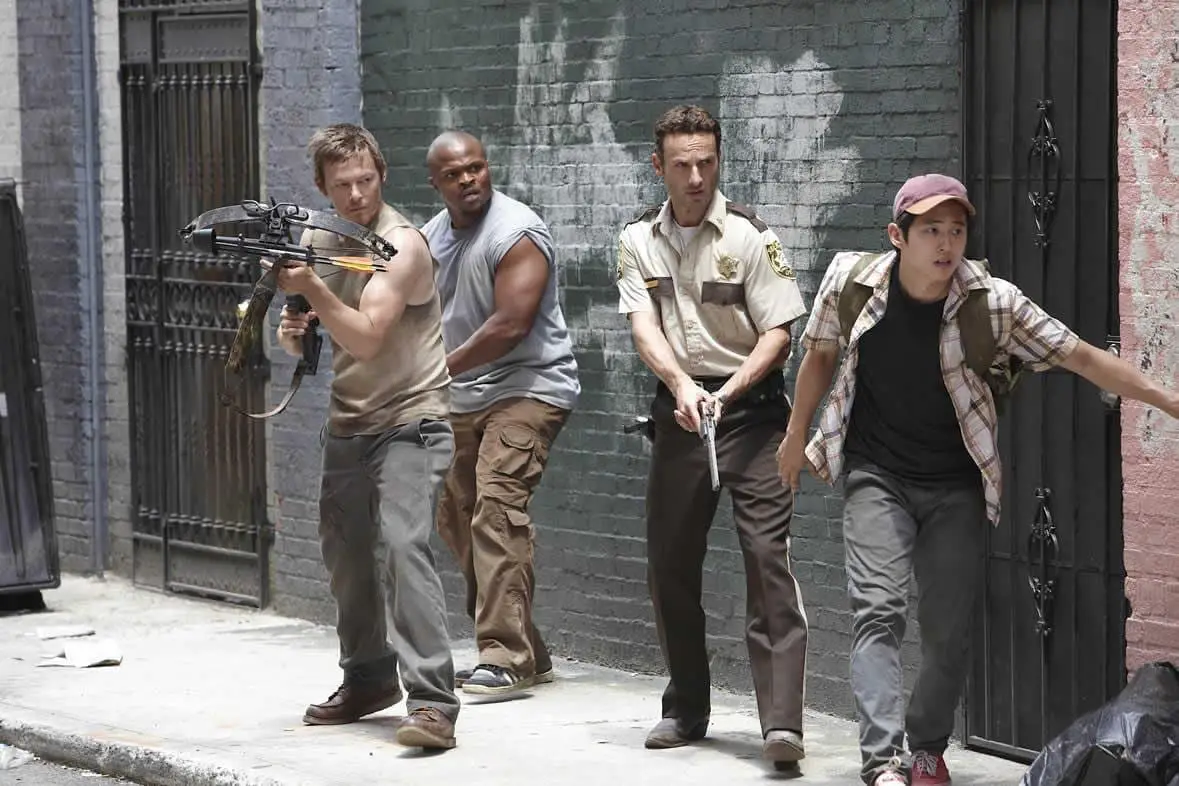 Rick and the gang edge to the corner of a building holding guns