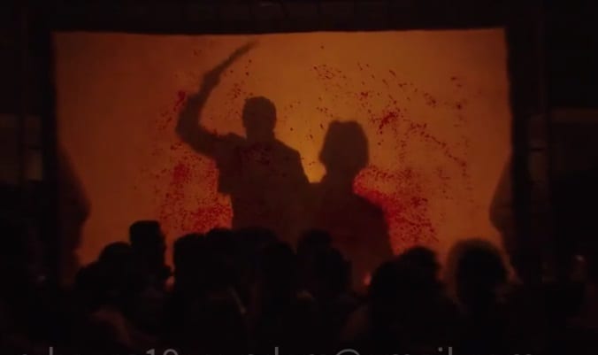 Shadows of a man attacking another with a machete appear on a blood soaked screen as a crowd of people scrambles in foreground.