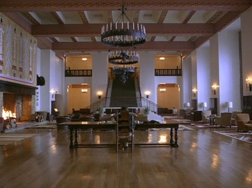 Long view of Overlook Hotel lobby as Jack Torrance sits in a highbacked chair working on writing.