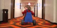 Danny Lloyd as Danny Torrance looks over his shoulder uneasily as he pedals down the hotel hallway on his tricycle.