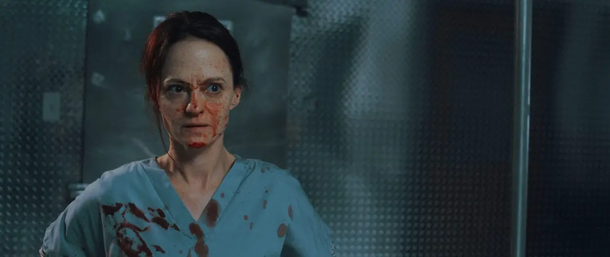 Mandy (Angela Bettis) stands in the morgue of a hospital in blood-stained scrubs.