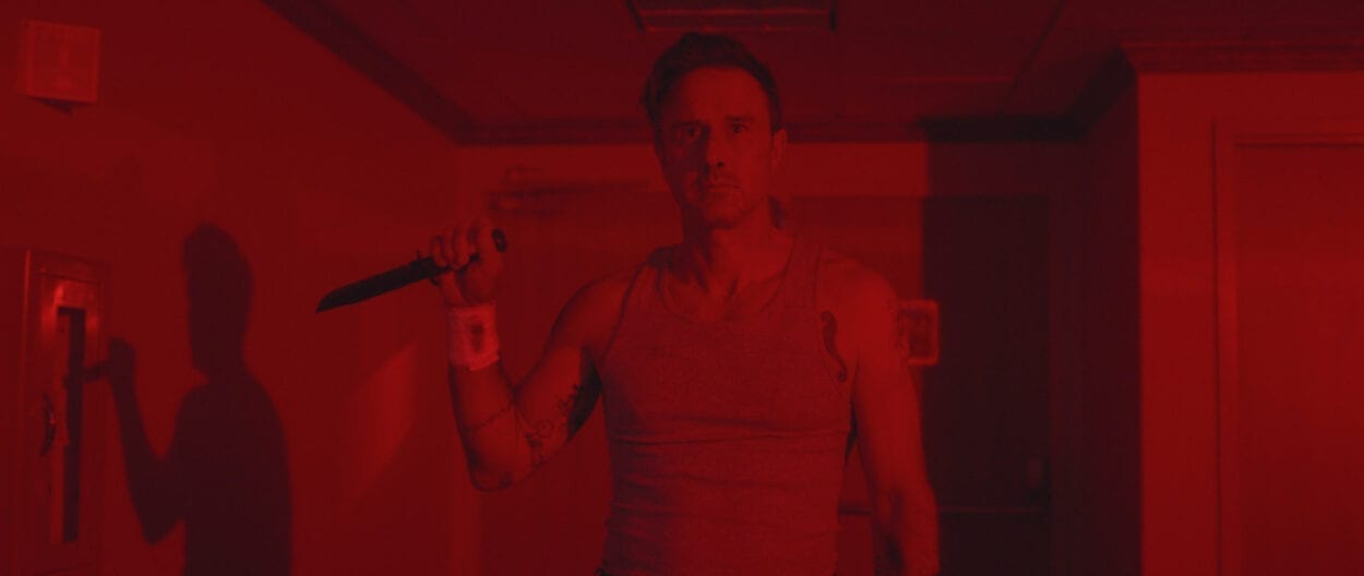 Jefferson (David Arquette) stands holding a knife in a red-lit room, wearing a wife beater.